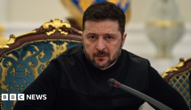 President of Ukraine Volodymyr Zelenskyy speaks at a meeting of the National Security and Defense Council on March 3, 2026 in Kyiv, Ukraine. He's leaning forward in his chair over a microphone, with a serious look on his face, and is dressed all in black