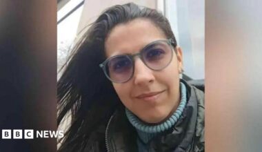 A picture shows the face of Barreto. She is wearing a blue turtleneck under a coat and glasses.