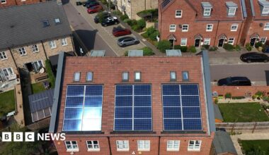 Aerial view of semi-detached and homes and terraced houses with solar panels installed. In the background are a series of avenues with cars parked up and small green lawns.