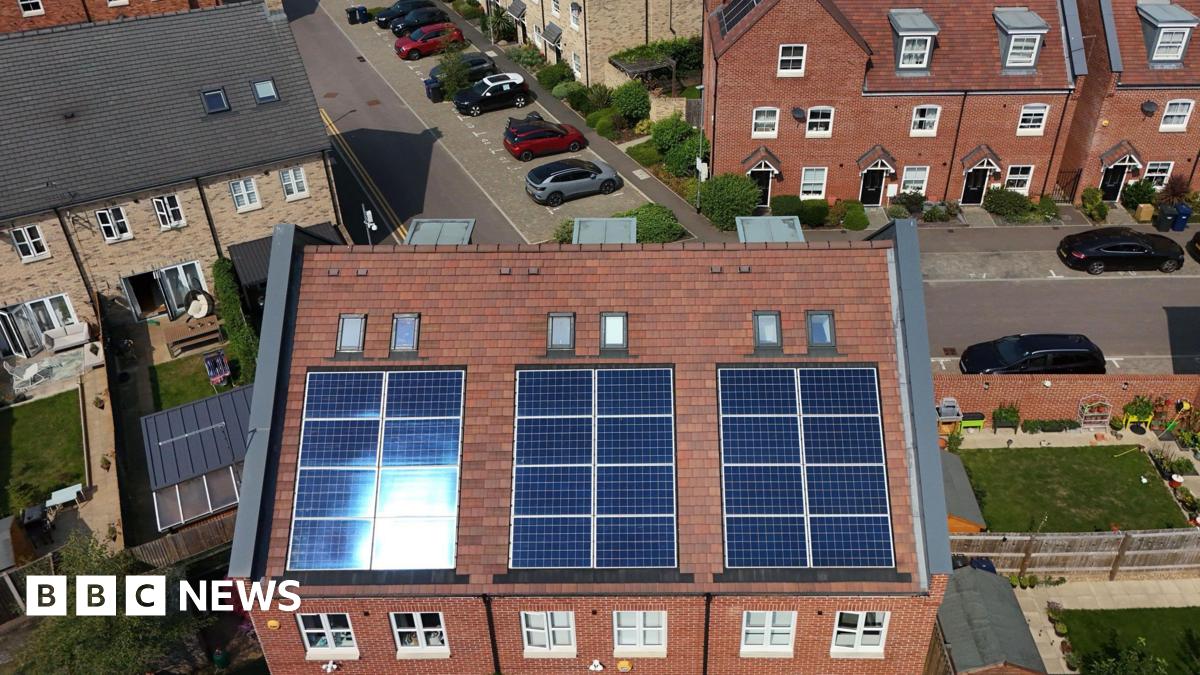 Aerial view of semi-detached and homes and terraced houses with solar panels installed. In the background are a series of avenues with cars parked up and small green lawns.