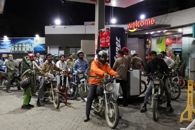 Dozens of motocycle riders dey queue at a petrol station for Karachi, Pakistan, on di night of 6 March 2026.