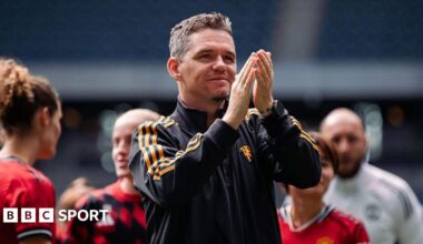 Marc Skinner, in black tracksuit top with orange stripes, applauds with players and staff in the background