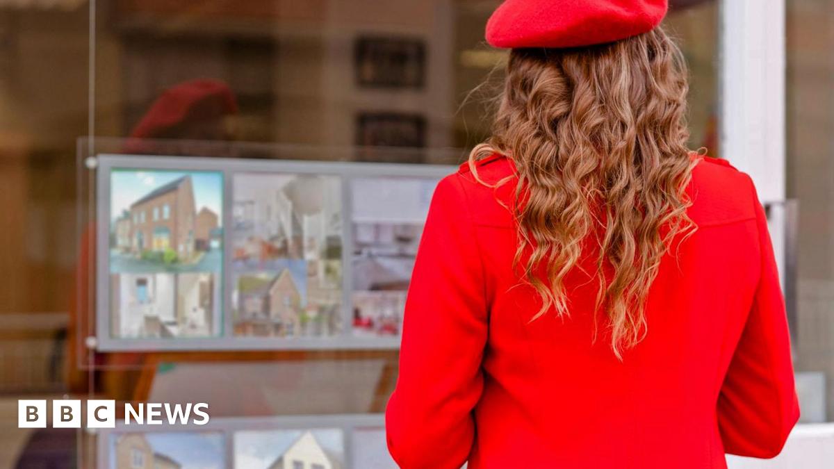 Woman wearing bright red beret and red coat faces an estate agent's window advertising homes for sale