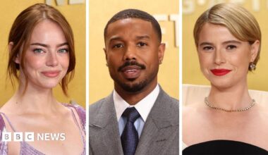 A woman with dark hair and a multiple colour jumper siting on a green sofa inside her living room.
