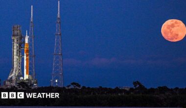 Artemis II rocket on the launch pad in Cape Canaveral with a full, bright and orange Moon rising in the sky next to it