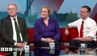 Damian Hinds, wearing a dark suit and green tie,  Zoe Franklin wearing a purple blouse and Tom Hayes wearing white shirt with sleeves rolled up on the a red TV studio sofa