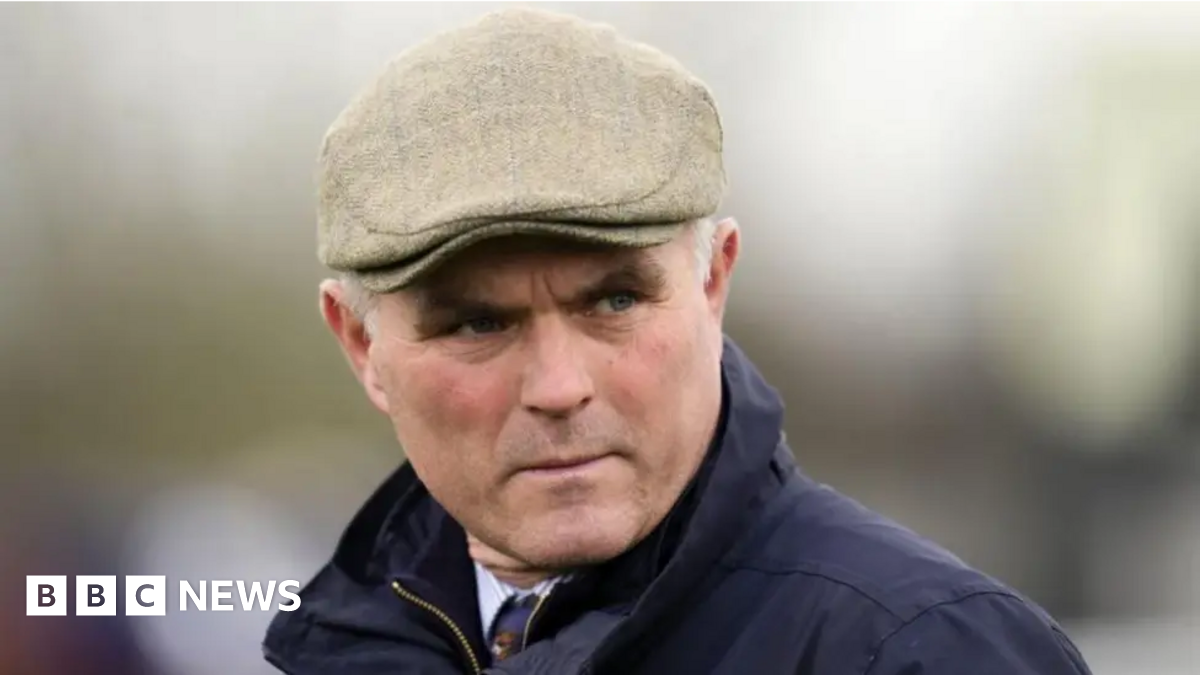Richard Evan Rhys Williams is pictured leaving Cardiff Crown Court. He is smiling through the sunshine, squinting slightly. He has grey short hair and wears a navy suit, white shirt and navy tie.
