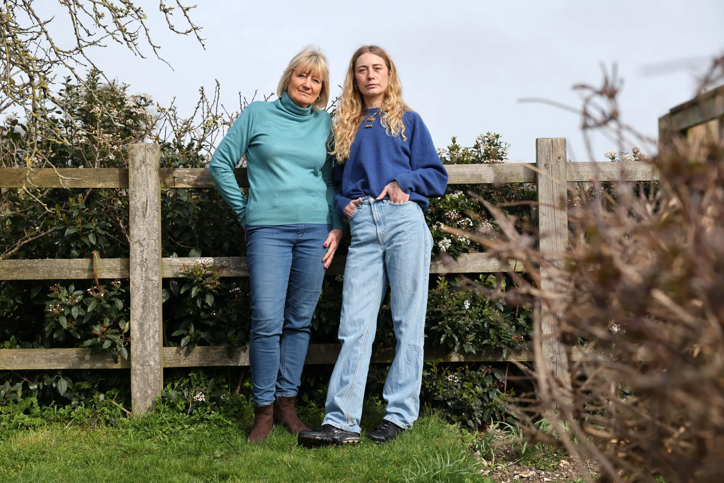 Tricia and Lara Monro, standing in a garden with a fence behind them.