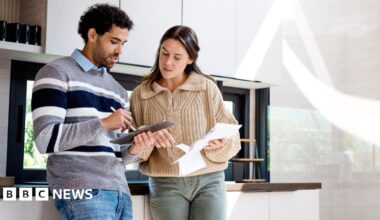 Couple in a kitchen look at a tablet and some paperwork.