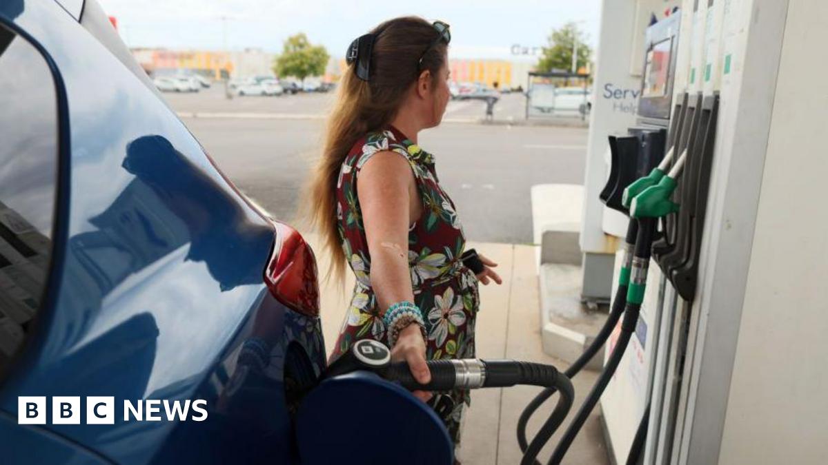 A woman in a floral dress fills her car at a petrol station.