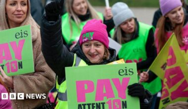 A woman with dark hair and a multiple colour jumper siting on a green sofa inside her living room.