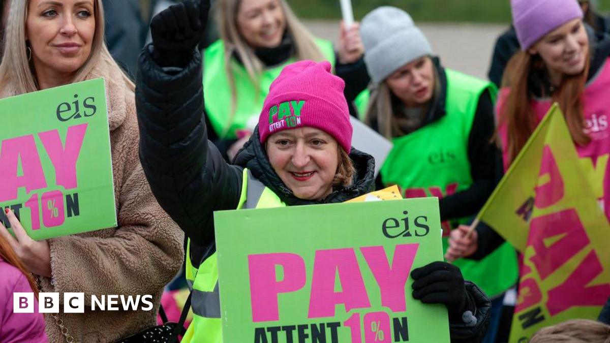 A woman with dark hair and a multiple colour jumper siting on a green sofa inside her living room.
