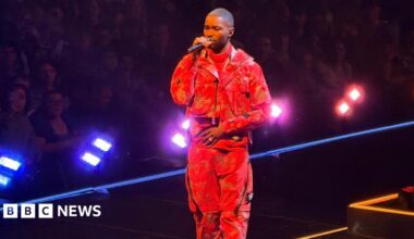 Dave performing with a microphone, wearing a red outfit