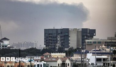 A woman with dark hair and a multiple colour jumper siting on a green sofa inside her living room.