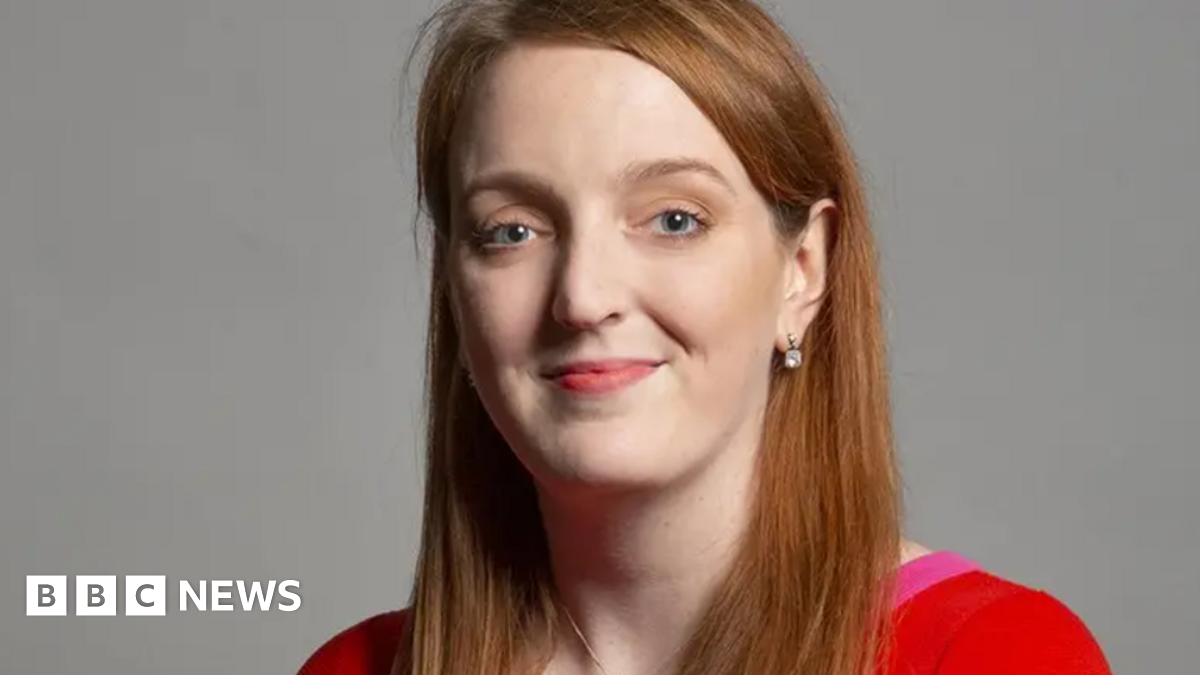 Portrait of Charlotte Nichols - Warrington North MP - with long red/light brown hair wearing a red and hot pink top. She is smiling.