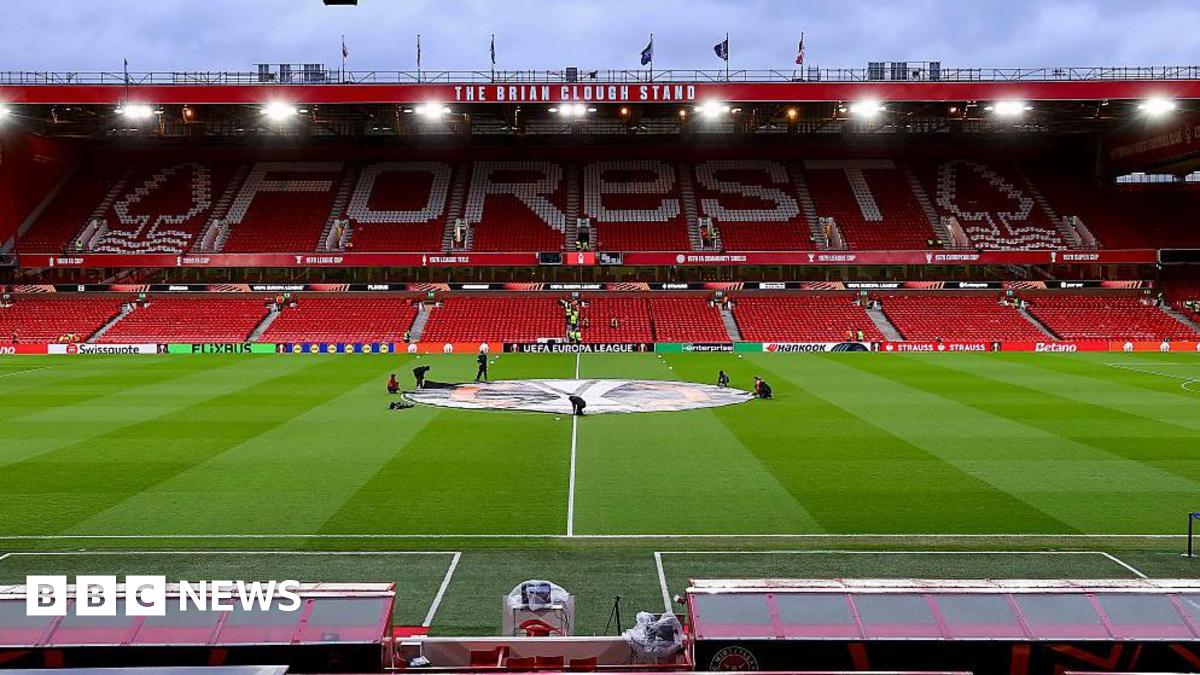 A low shot of the Nottingham Forest home pitch, with a tall, red and white football stand in the background