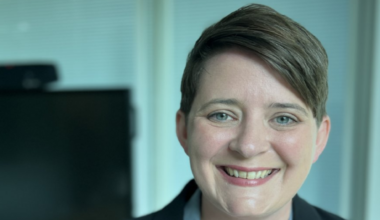 Headshot of education minister Olivia Bailey. She wears her cropped brown hair parted and swept to one side. She is wearing a powder-blue shirt and a black jacket.
