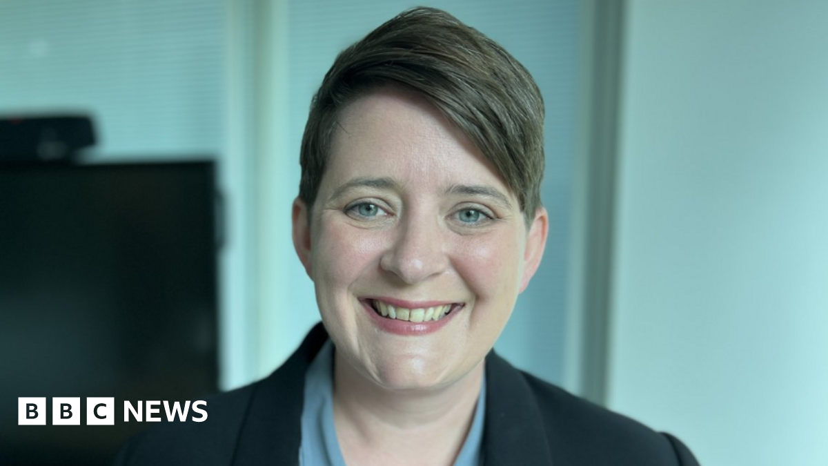 Headshot of education minister Olivia Bailey. She wears her cropped brown hair parted and swept to one side. She is wearing a powder-blue shirt and a black jacket.