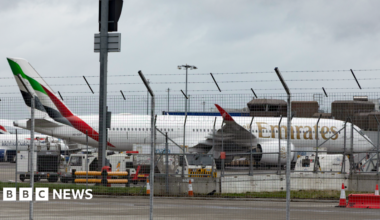 Emirates plane at Edinburgh Airport. It is behind a metal fence with other planes behind it.