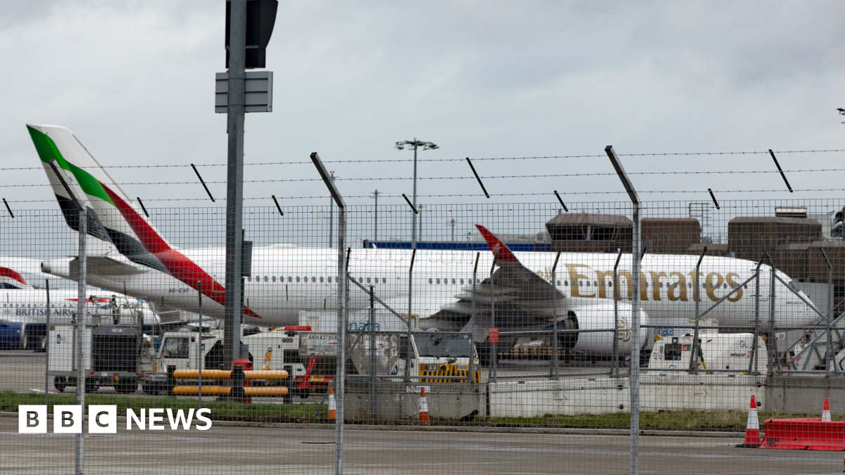 Emirates plane at Edinburgh Airport. It is behind a metal fence with other planes behind it.