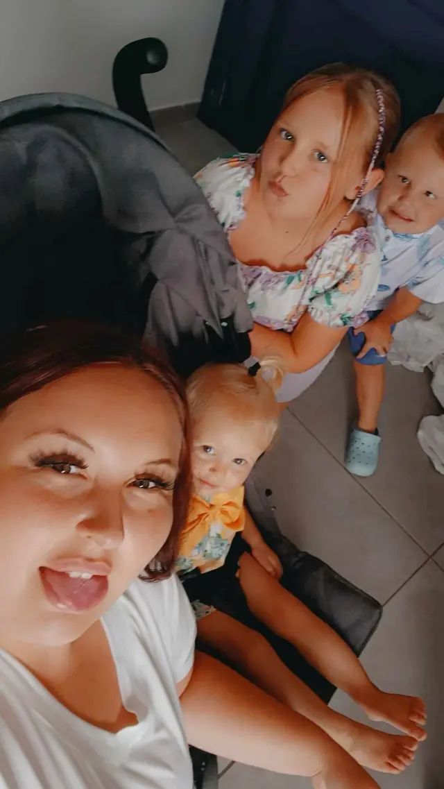 A woman and three young children look up at the camera as they take a selfie