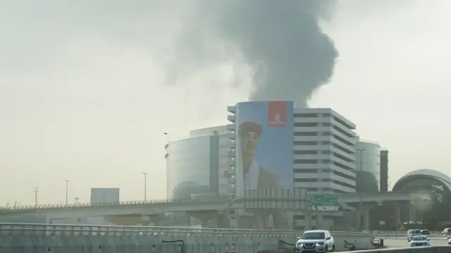 Smoke rising from near the Dubai International Airport is seen through the windshield of a vehicle.
