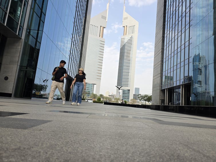 a young man and woman walk past an otherwise deserted nasdaq dubai in dubai financial centre in the UAE.