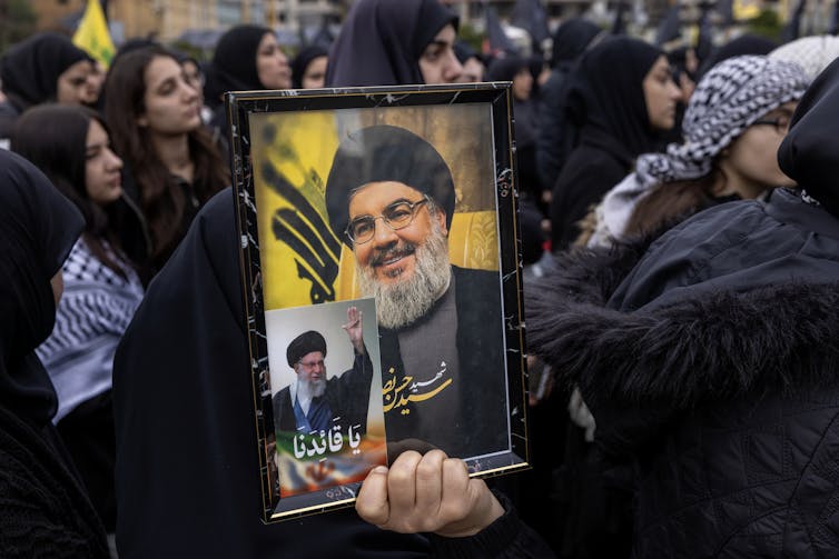 A photo of a man with a beard is held by a woman.