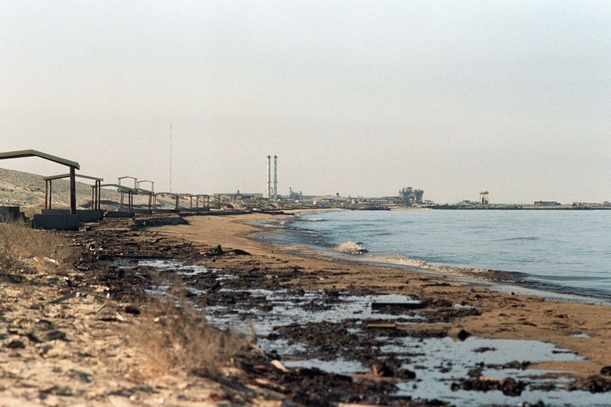 Oil washed up on a beach near the Kuwait-Saudi border, while a closed Saudi desalination plant looms in the background, on January 29, 1991.