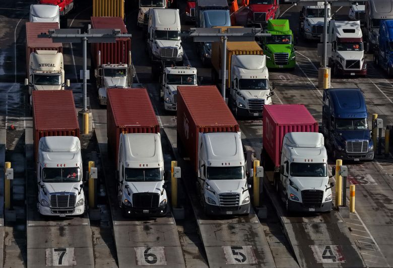 In an aerial view, trucks carrying shipping containers line up to enter a shipping berth at the Port of Oakland on January 28, 2026 in Oakland, California.