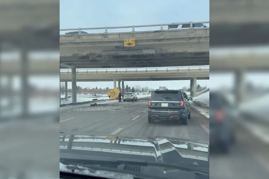 The view from a car travelling on Highway 11 with a damaged overpass overhead. Another vehicle is in front and some equipment parts are in the median ditch.