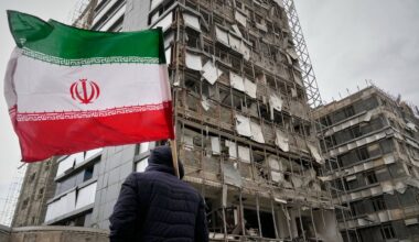 A man holds an Iranian flag as he looks at the damaged façade of Gandhi Hospital, which was hit Sunday when a strike also struck a state TV communications tower and nearby buildings across the street during the ongoing joint U.S. Israeli military campaign in Tehran, Iran, Monday, March 2, 2026. (AP Photo/Vahid Salemi)