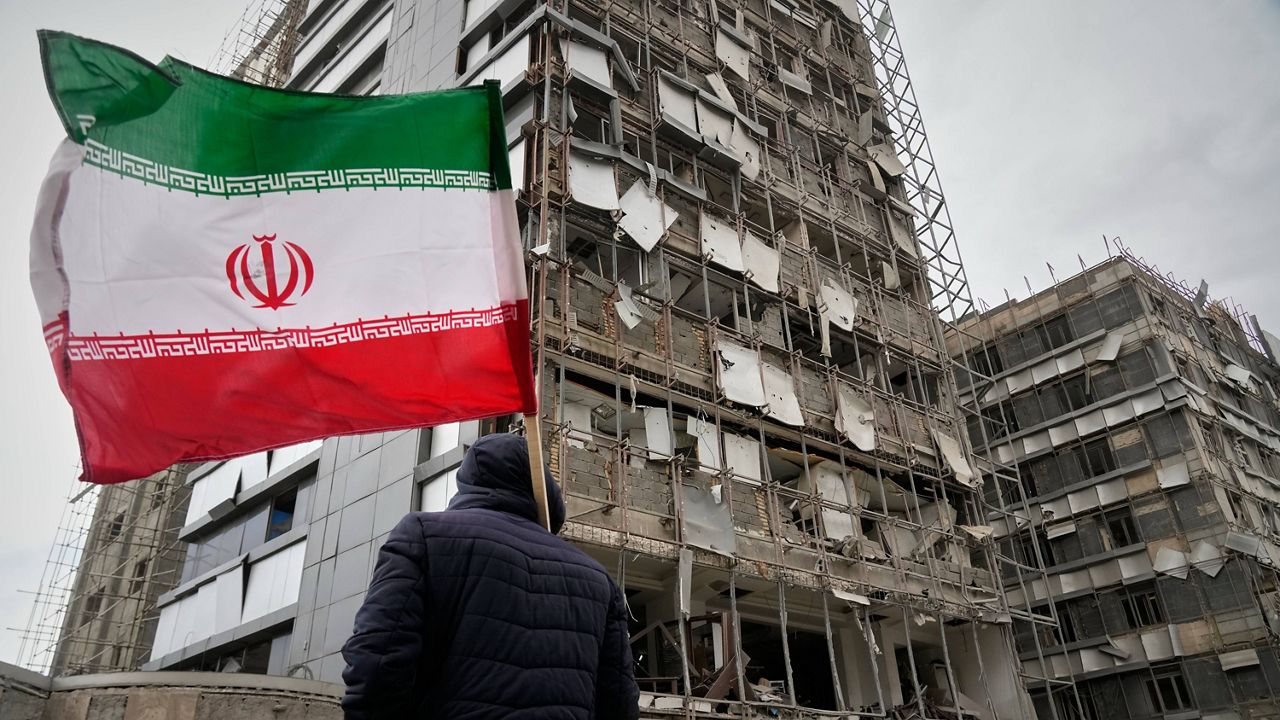 A man holds an Iranian flag as he looks at the damaged façade of Gandhi Hospital, which was hit Sunday when a strike also struck a state TV communications tower and nearby buildings across the street during the ongoing joint U.S. Israeli military campaign in Tehran, Iran, Monday, March 2, 2026. (AP Photo/Vahid Salemi)