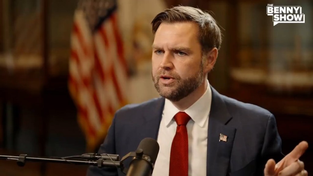 JD Vance speaking with a microphone in front of an American flag.