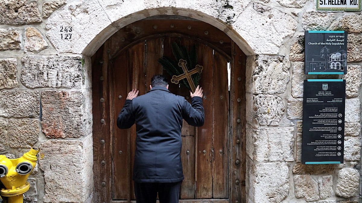 a man bows his head in front of a locked house of worship door