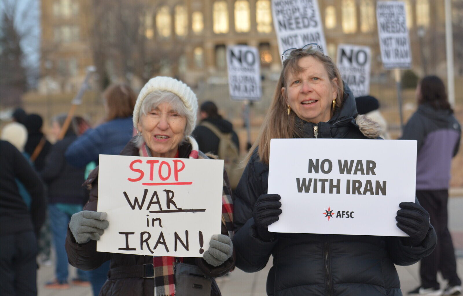 2 people holding signs opposing war with Iran