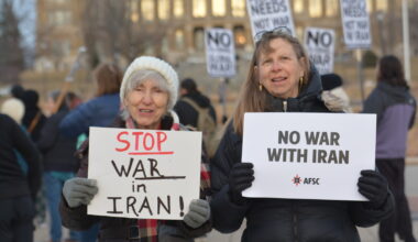 2 people holding signs opposing war with Iran