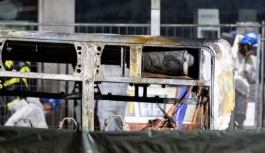 Fire investigators examine the charred shell of a bus that caught fire. Pic: AP