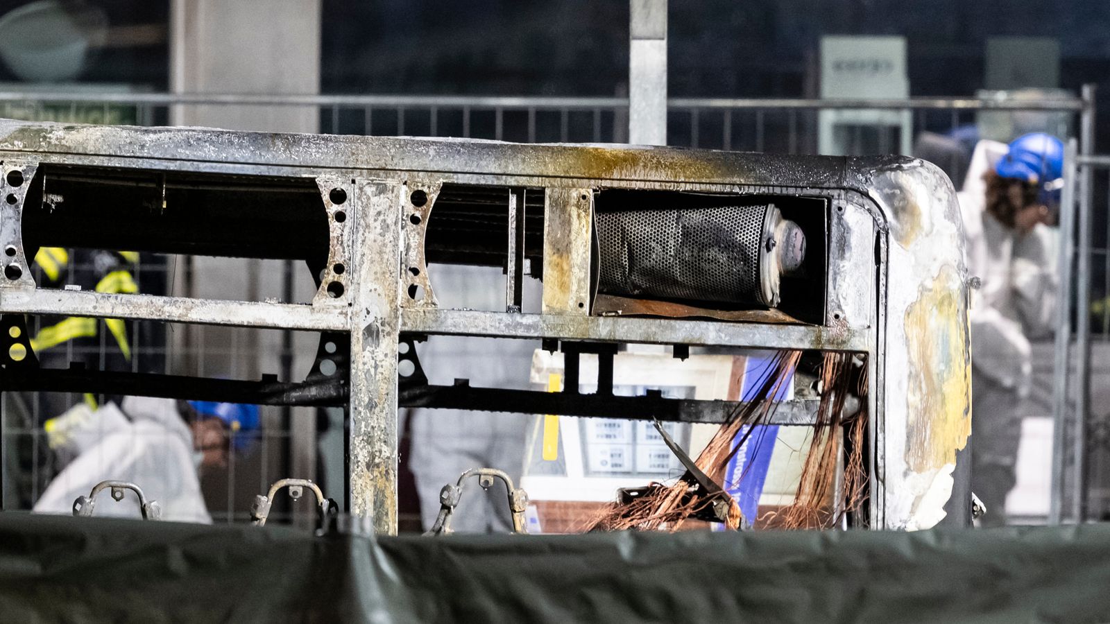 Fire investigators examine the charred shell of a bus that caught fire. Pic: AP