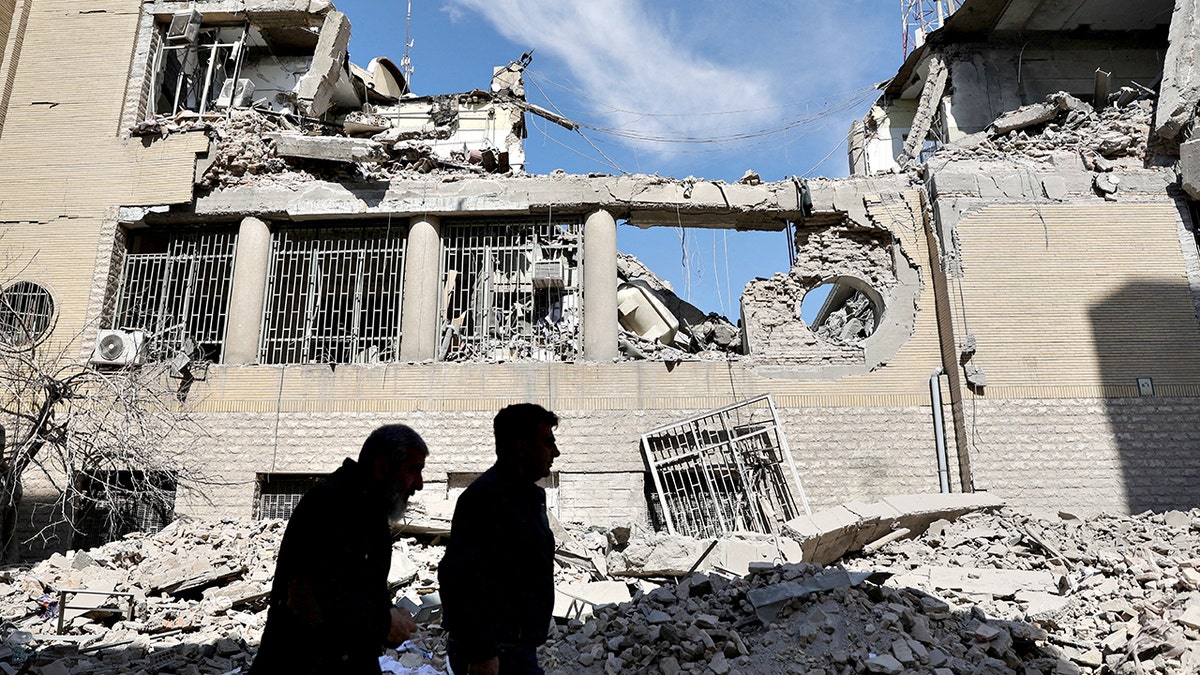 People walk past damaged buildings