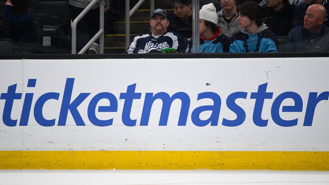 A large Ticketmaster logo on the boards inside an ice hockey arena.