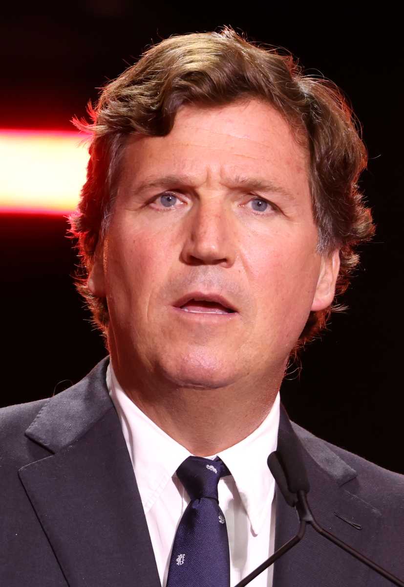 Tucker Carlson speaking at a microphone
