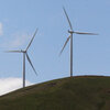 Seven modern windmills with three blades each stand along a hillside.