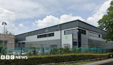 An image of a large black and grey building with a smaller light brown building on the left side covered in satellite dishes.
