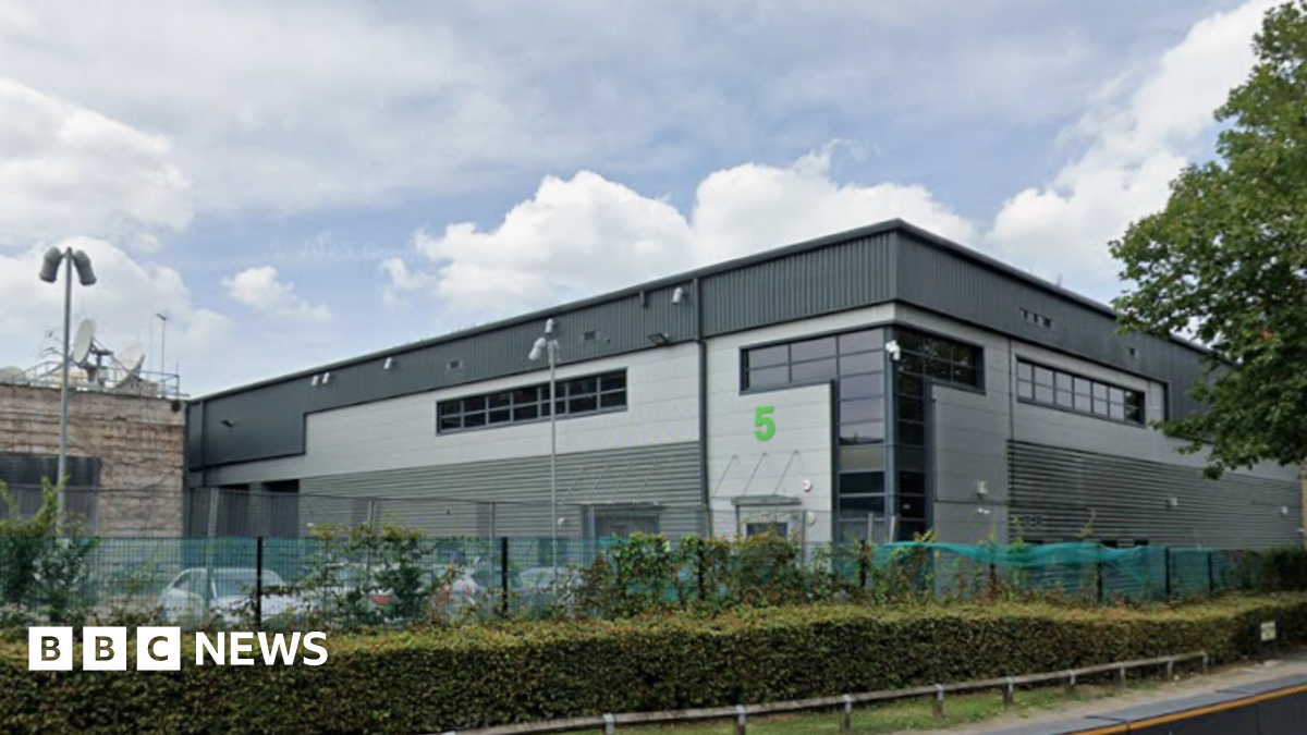 An image of a large black and grey building with a smaller light brown building on the left side covered in satellite dishes.