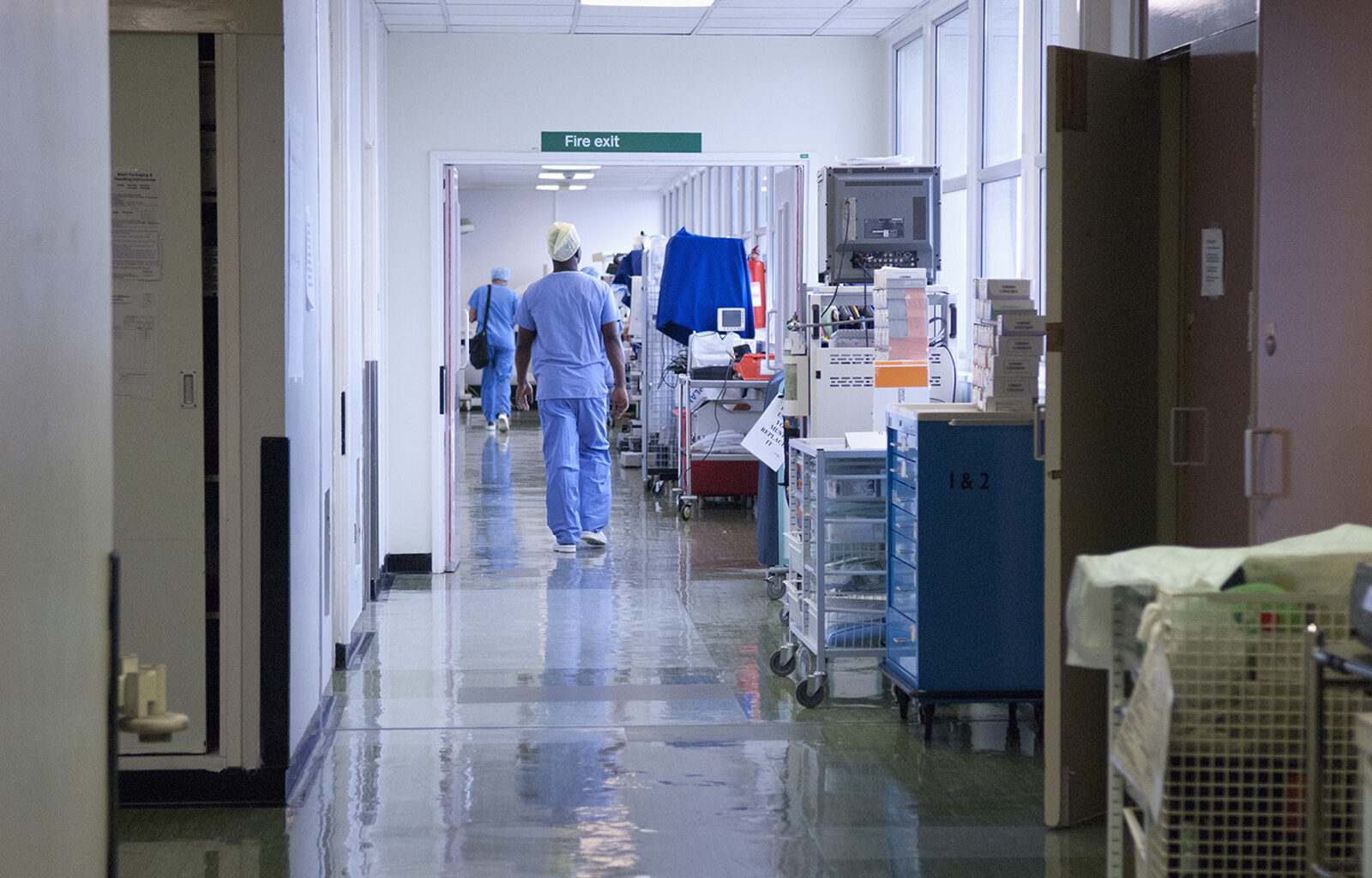 A stock image of a hospital corridor, with two health workers in sanitary clothing walking away from the camera