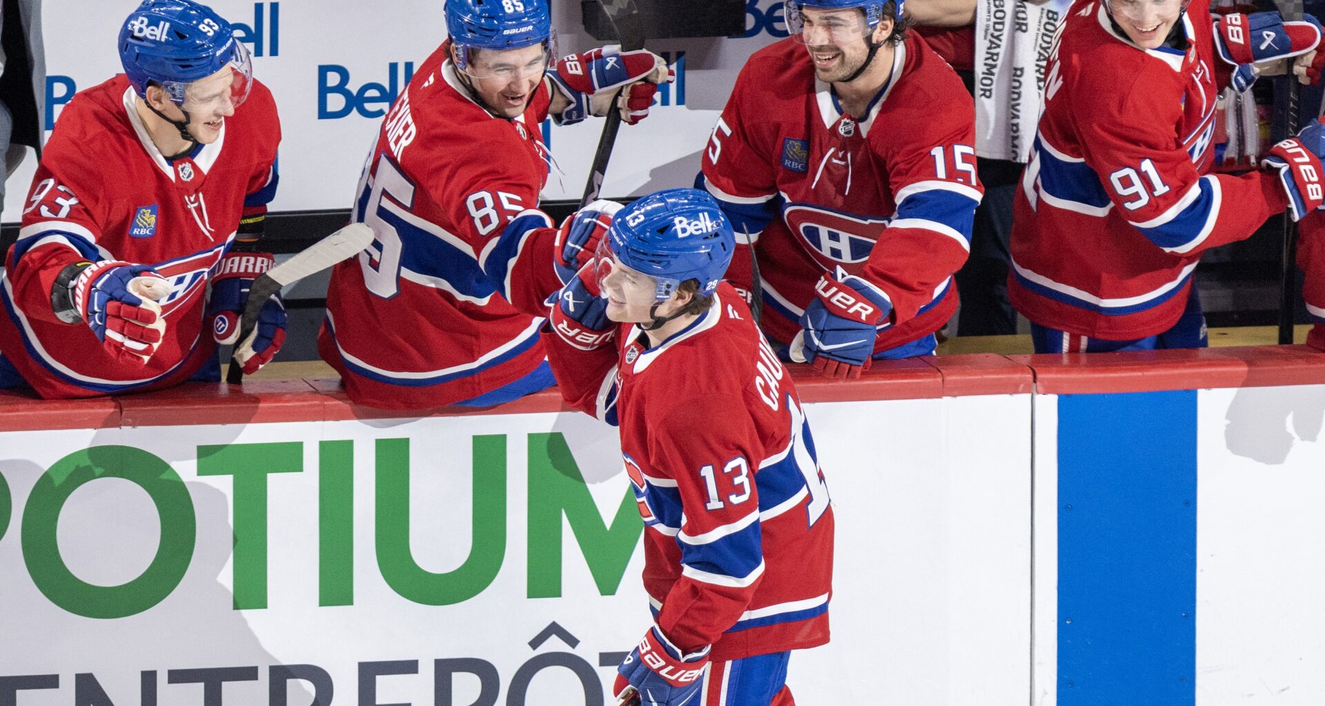 Hockey players on the bench congratulate a teammate skating by after he scored a goal.
