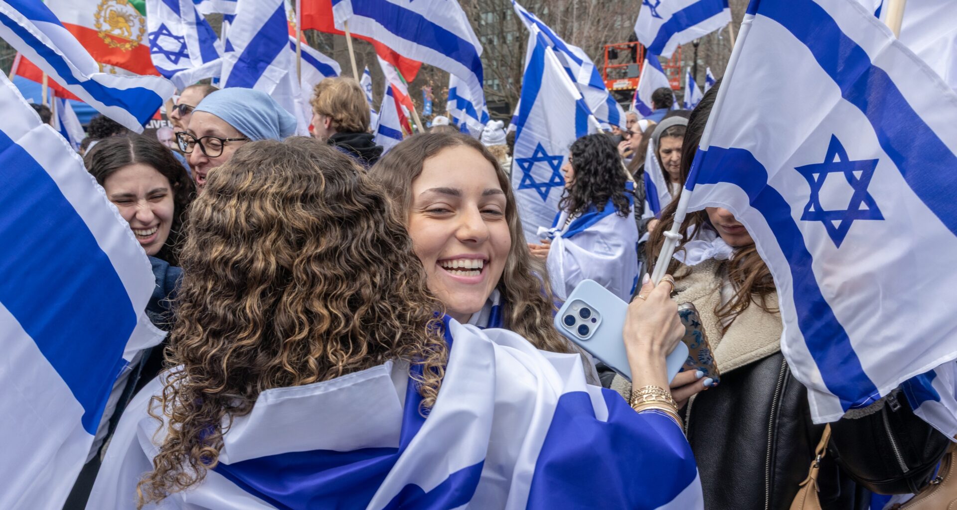 Two girls hug amid a throng of people carrying the Israeli flag.
