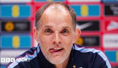 Head and shoulders view of England head coach Thomas Tuchel at a news conference, with his tongue poking out of his mouth