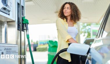 A woman wearing a white top and yellow shirt looks at a pump while filling up her car.